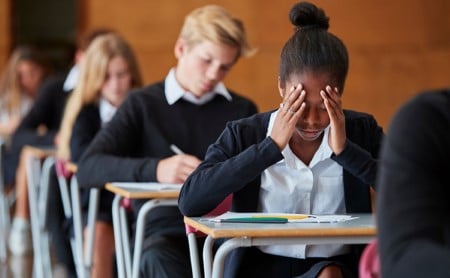 A Black high school student concentrating on her test, her peers are testing, as well.