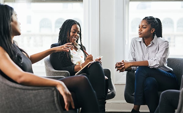 Three Black women engaged in a serious discussion during a meeting