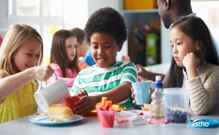 Three elementary school children smiling during a healthy lunch