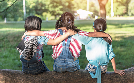 Three girls sitting on a log with their arms around each other's shoulders