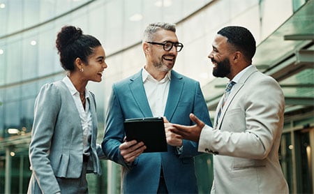 Three business professionals talking outside a glass office building.
