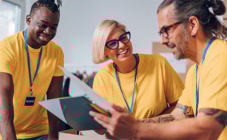 Three volunteers in yellow T-shirts smiling and discussing documents.