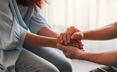 Two people holding hands while seated, comforting each other.