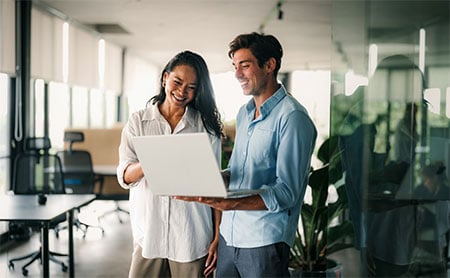 Two people in an office looking at a laptop together.