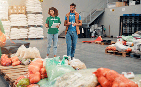 Two volunteers in a warehouse with packaged goods on pallets.