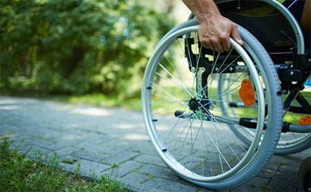 wheelchair-moving-on-sidewalk-grassy-park.jpg