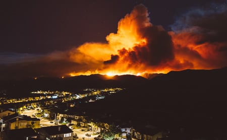 A large wildfire looms over a subsurban street at night