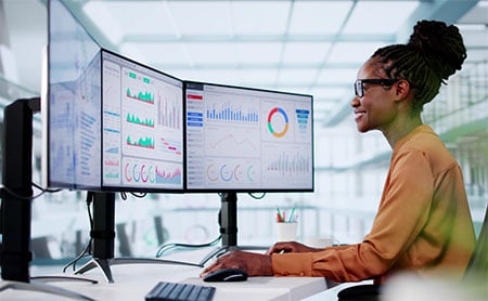 Person analyzing data on dual monitors in a modern office setting.