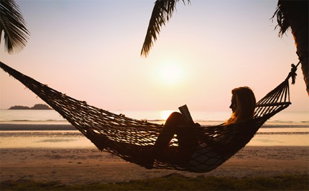 Woman reading in a hammock on a tropical beach at sunset