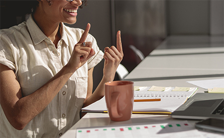 A woman smiles while signing during a virtual meeting