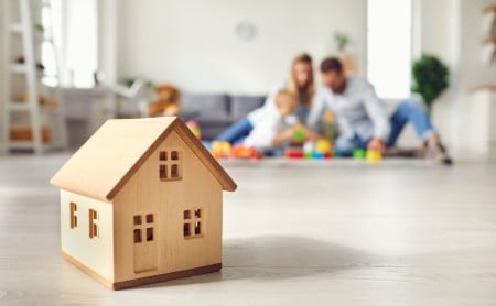 Closeup of wooden toy house, blurred family playing in the background