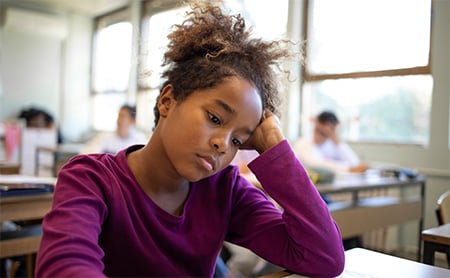 A young Black girl sits sadly at her school desk