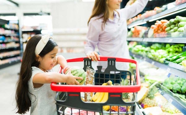 Young girl helping her mother with grocery shopping by adding food to their shopping cart